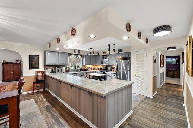 kitchen with gray cabinetry, dark wood-type flooring, tasteful backsplash, kitchen peninsula, and stainless steel appliances