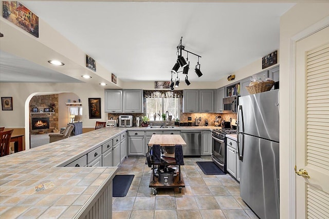 kitchen with tile countertops, sink, hanging light fixtures, gray cabinets, and appliances with stainless steel finishes