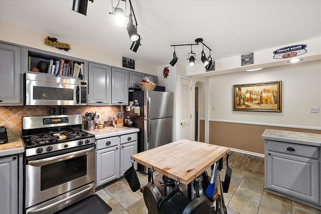 kitchen with gray cabinetry, backsplash, stainless steel appliances, and hanging light fixtures