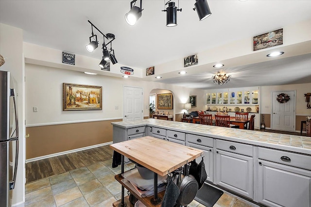 kitchen with tile countertops, gray cabinets, and stainless steel refrigerator