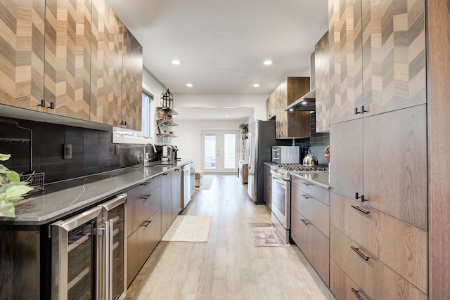 kitchen featuring decorative backsplash, appliances with stainless steel finishes, wall chimney exhaust hood, beverage cooler, and sink