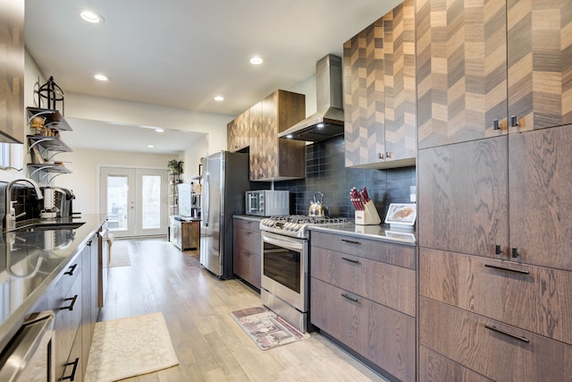 kitchen with decorative backsplash, french doors, stainless steel appliances, sink, and wall chimney range hood