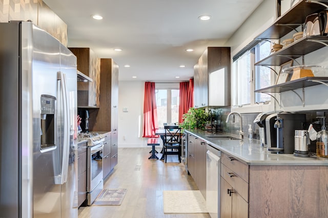 kitchen featuring backsplash, stainless steel appliances, sink, light hardwood / wood-style flooring, and range hood