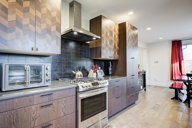 kitchen with backsplash, island exhaust hood, stainless steel range with gas cooktop, and light wood-type flooring