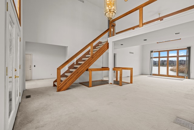 unfurnished living room featuring a notable chandelier, light colored carpet, and a high ceiling