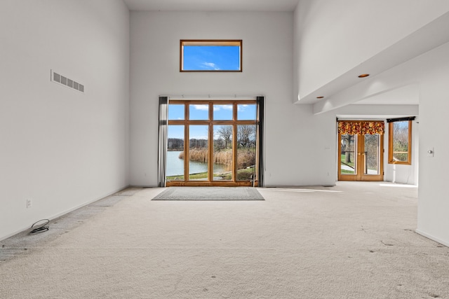 unfurnished living room with light carpet, a high ceiling, and a water view