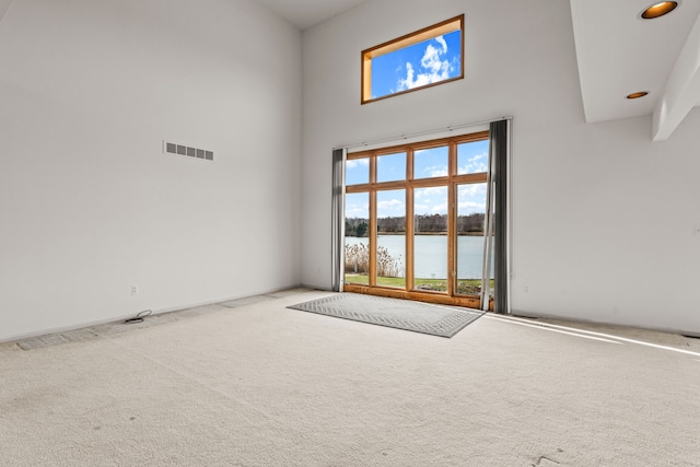 unfurnished room with a high ceiling, carpet floors, a water view, and a healthy amount of sunlight