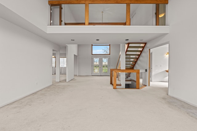 unfurnished living room with carpet flooring, a high ceiling, and french doors