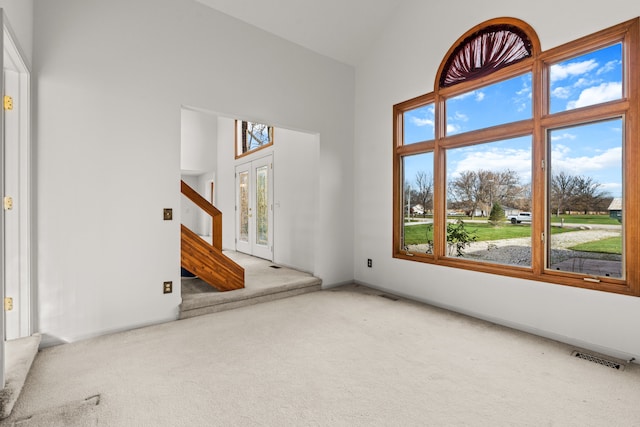 carpeted empty room with french doors, high vaulted ceiling, and a healthy amount of sunlight