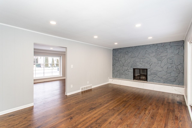 unfurnished living room with dark wood-type flooring, ornamental molding, and a stone fireplace