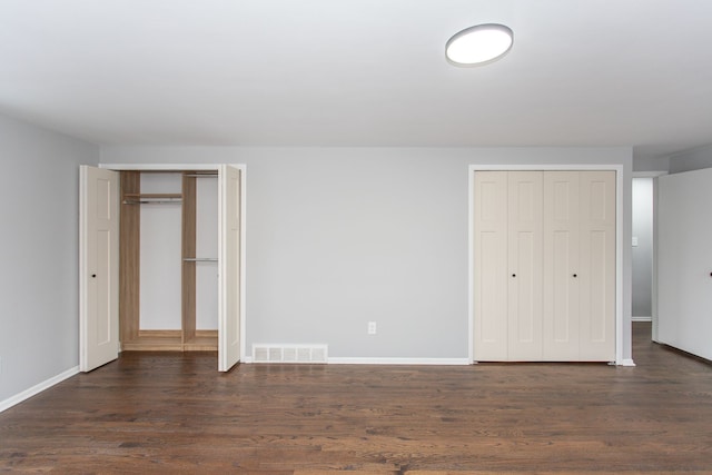 unfurnished bedroom featuring dark hardwood / wood-style flooring and multiple closets