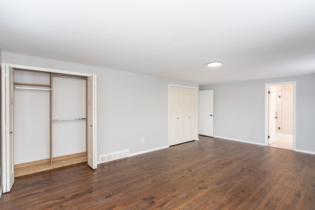 unfurnished bedroom with multiple closets and dark hardwood / wood-style floors