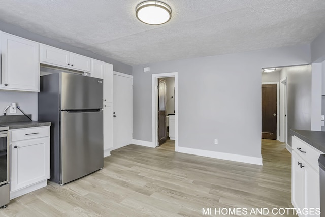 kitchen featuring stove, a textured ceiling, light hardwood / wood-style floors, white cabinetry, and stainless steel refrigerator