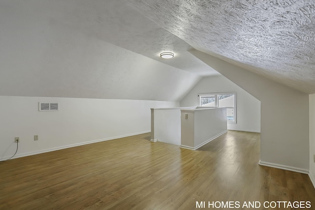 additional living space featuring hardwood / wood-style floors, a textured ceiling, and vaulted ceiling