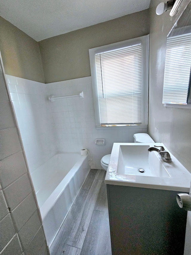 bathroom with vanity, hardwood / wood-style flooring, toilet, a tub to relax in, and tile walls