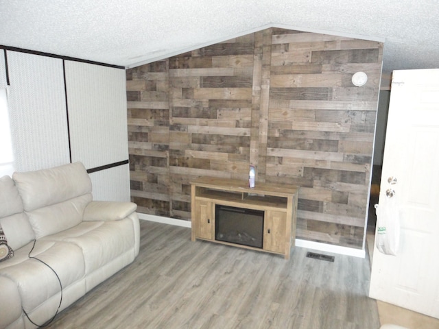 living room with lofted ceiling, wooden walls, hardwood / wood-style flooring, a fireplace, and a textured ceiling