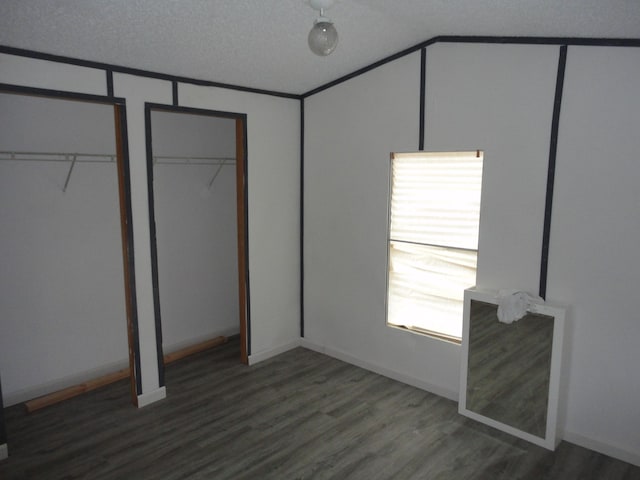 unfurnished bedroom featuring multiple closets, a textured ceiling, and dark wood-type flooring