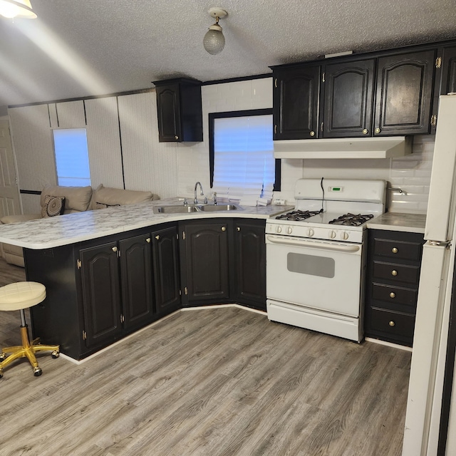 kitchen featuring sink, white appliances, light hardwood / wood-style floors, kitchen peninsula, and a textured ceiling