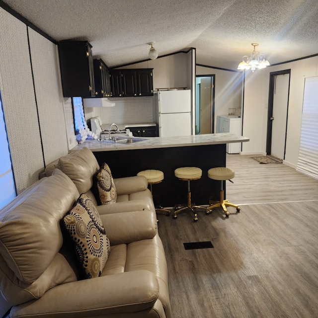 kitchen featuring a breakfast bar, washer / dryer, kitchen peninsula, white fridge, and light hardwood / wood-style floors