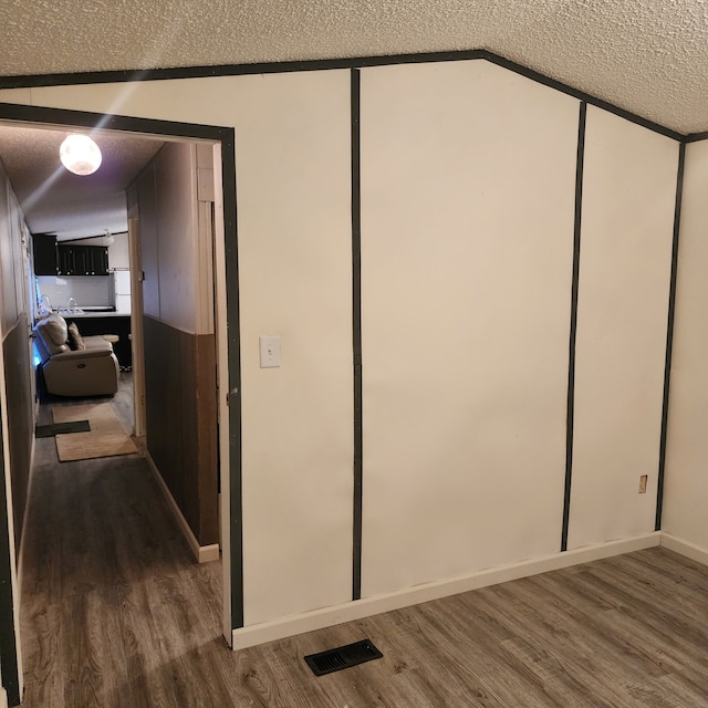 interior space featuring hardwood / wood-style flooring, lofted ceiling, and a textured ceiling