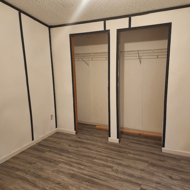 unfurnished bedroom featuring two closets, dark hardwood / wood-style floors, and a textured ceiling