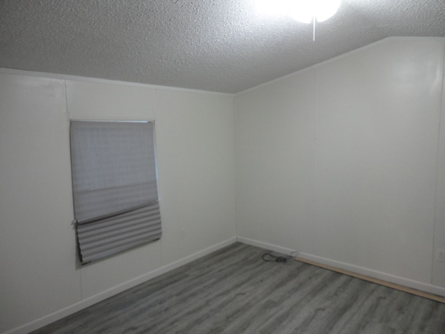 spare room with vaulted ceiling, hardwood / wood-style floors, and a textured ceiling