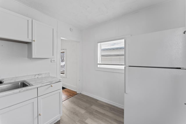 kitchen with white cabinets, white fridge, light hardwood / wood-style floors, and sink