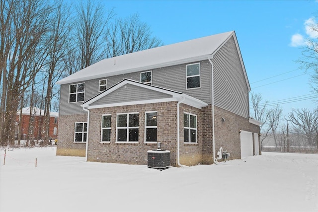 snow covered rear of property featuring central AC unit and a garage