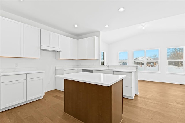 kitchen with vaulted ceiling, a kitchen island, sink, white cabinets, and light hardwood / wood-style flooring