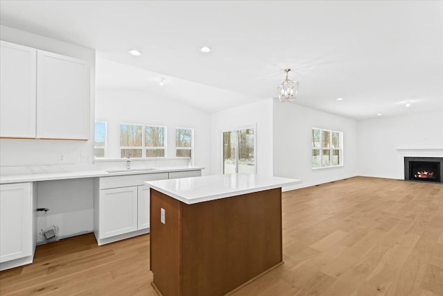 kitchen with sink, white cabinetry, decorative light fixtures, vaulted ceiling, and light hardwood / wood-style floors