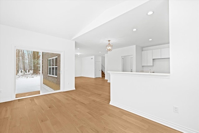 unfurnished living room with a chandelier, vaulted ceiling, and light wood-type flooring