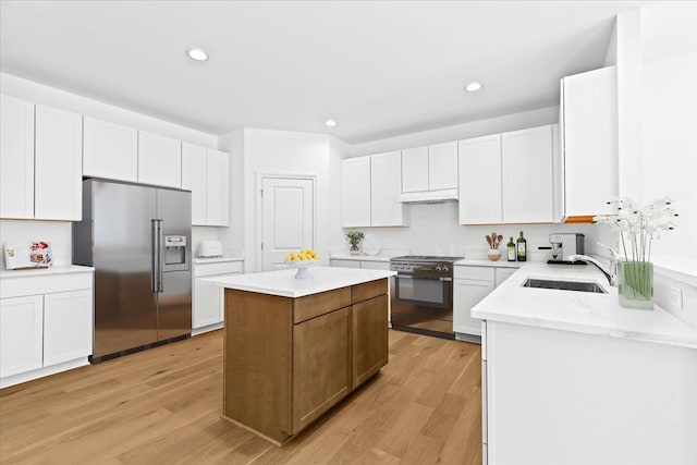 kitchen with a kitchen island, white cabinetry, sink, high end appliances, and light hardwood / wood-style floors