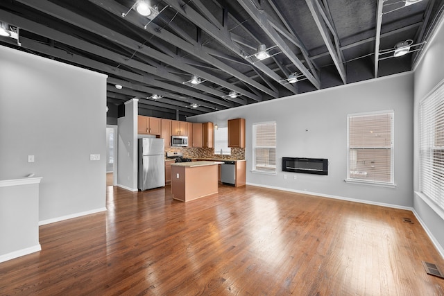 kitchen with stainless steel appliances, backsplash, hanging light fixtures, a kitchen island, and dark wood-type flooring