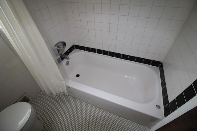 bathroom with toilet, tile walls, and tile patterned floors