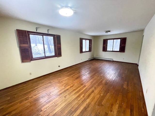 spare room featuring a healthy amount of sunlight, hardwood / wood-style floors, and a baseboard radiator