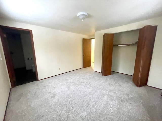 unfurnished bedroom with ensuite bath, a closet, and light colored carpet