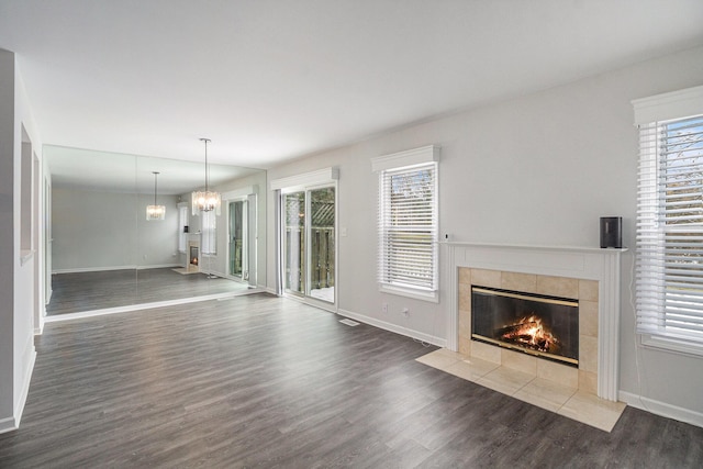 unfurnished living room with dark hardwood / wood-style floors, a chandelier, and a tiled fireplace