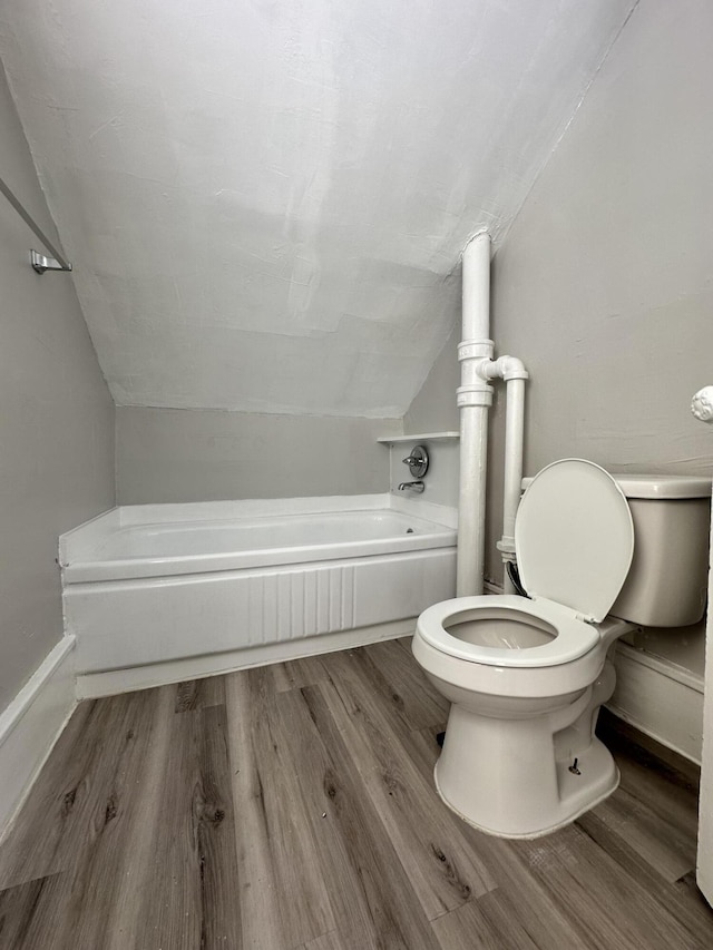 bathroom featuring a bathing tub, hardwood / wood-style floors, lofted ceiling, and toilet