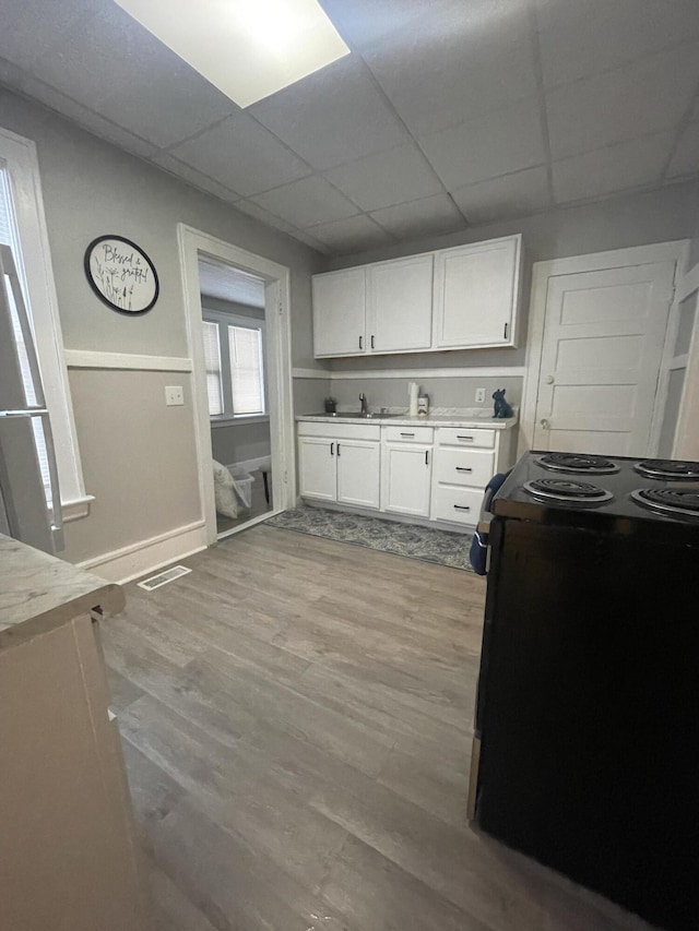 kitchen with a paneled ceiling, sink, black electric range, light hardwood / wood-style floors, and white cabinetry