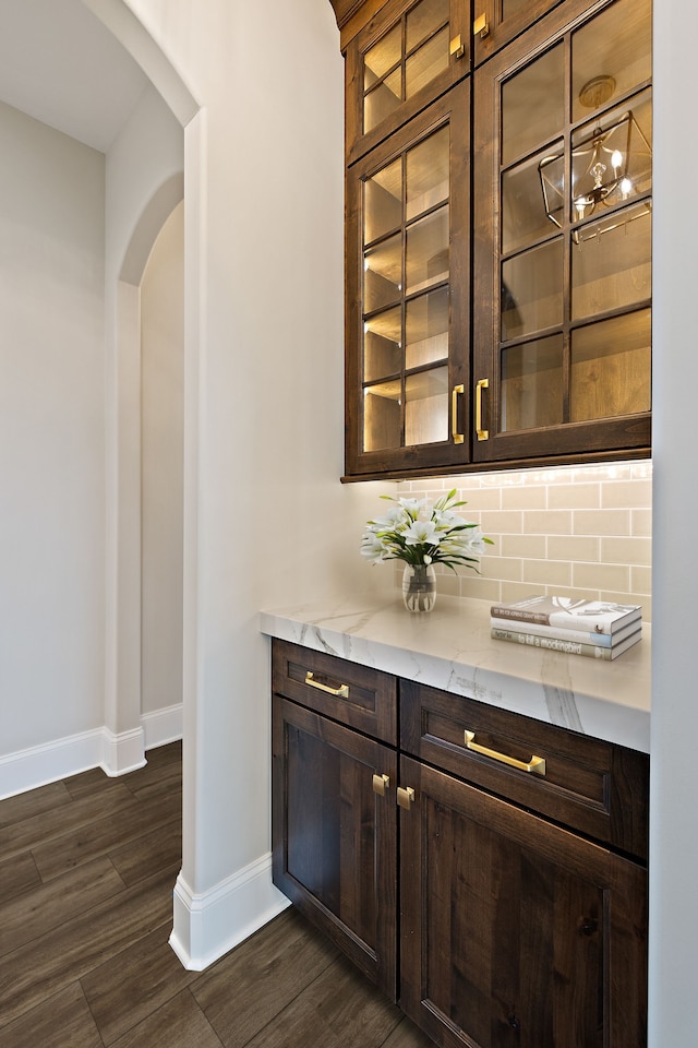 bar featuring decorative backsplash, dark brown cabinetry, dark hardwood / wood-style floors, and light stone countertops