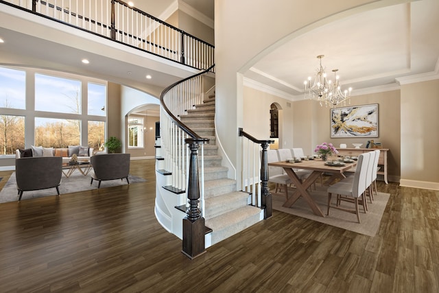 staircase featuring hardwood / wood-style floors, a towering ceiling, ornamental molding, and an inviting chandelier