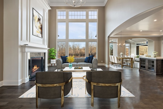 living room featuring crown molding, a towering ceiling, dark wood-type flooring, and a chandelier