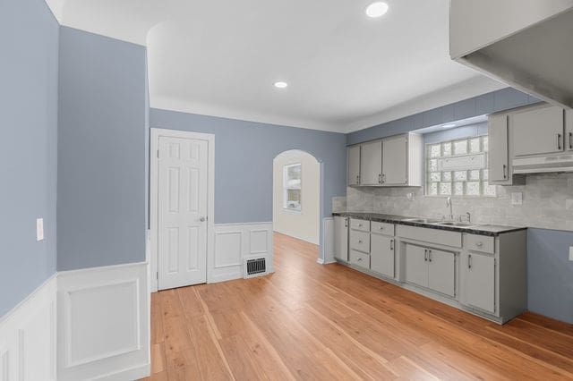 kitchen with tasteful backsplash, gray cabinetry, sink, and light hardwood / wood-style floors