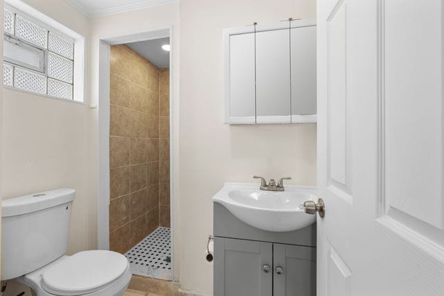 bathroom with vanity, crown molding, tile patterned flooring, toilet, and tiled shower