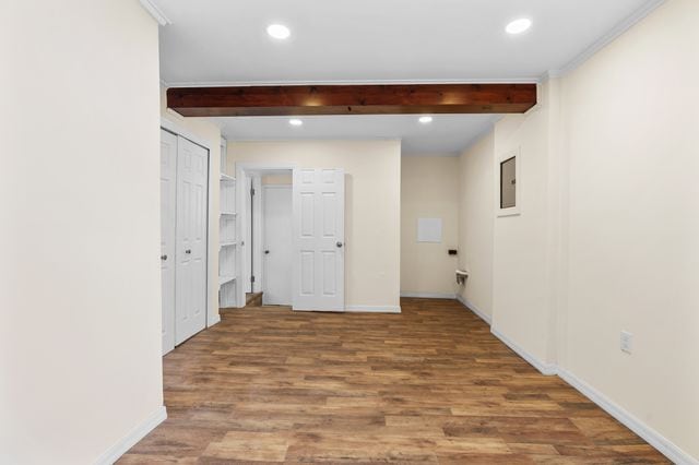 corridor featuring hardwood / wood-style floors, ornamental molding, beamed ceiling, and electric panel