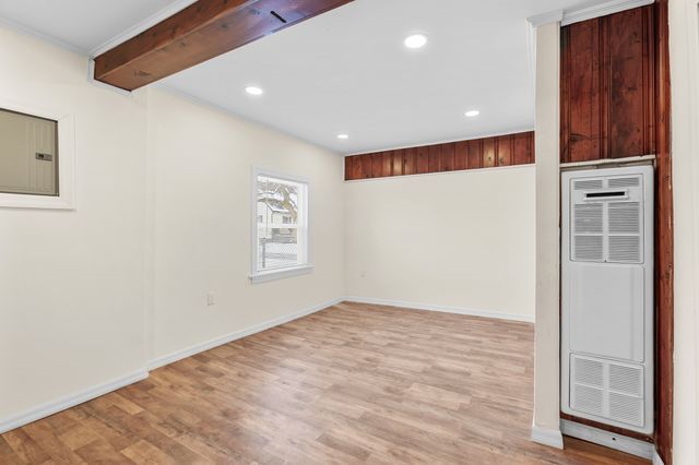 spare room with beam ceiling, electric panel, ornamental molding, and light wood-type flooring