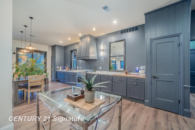 kitchen with gray cabinets, hanging light fixtures, light wood-type flooring, and custom exhaust hood