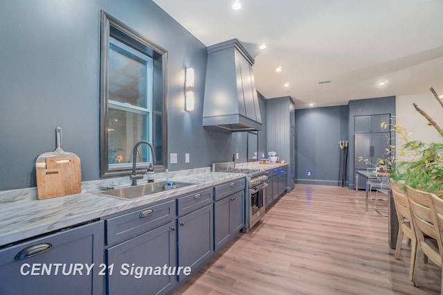 kitchen featuring sink, high end stainless steel range oven, light hardwood / wood-style flooring, wall chimney exhaust hood, and light stone countertops