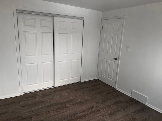 unfurnished bedroom with a closet, visible vents, baseboards, and dark wood-style flooring