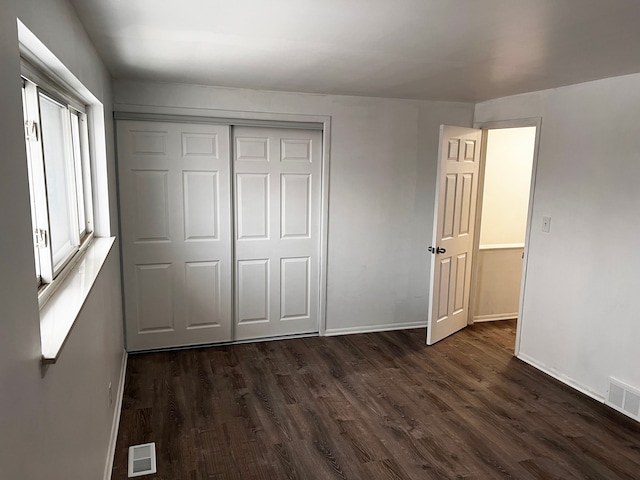 unfurnished bedroom with visible vents, baseboards, a closet, and dark wood-style floors